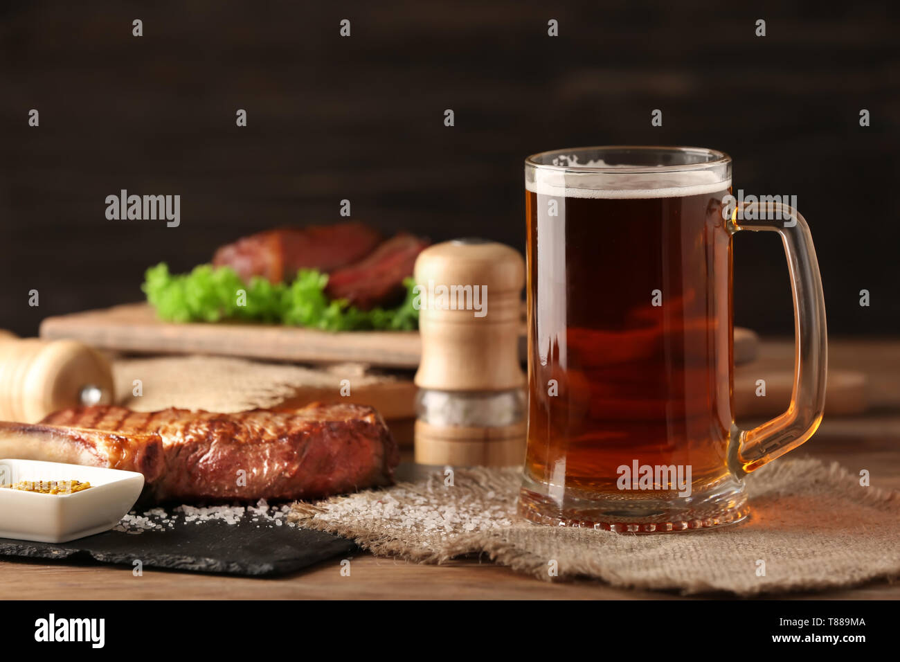 Mug of delicious beer with grilled steak on wooden table Stock Photo ...