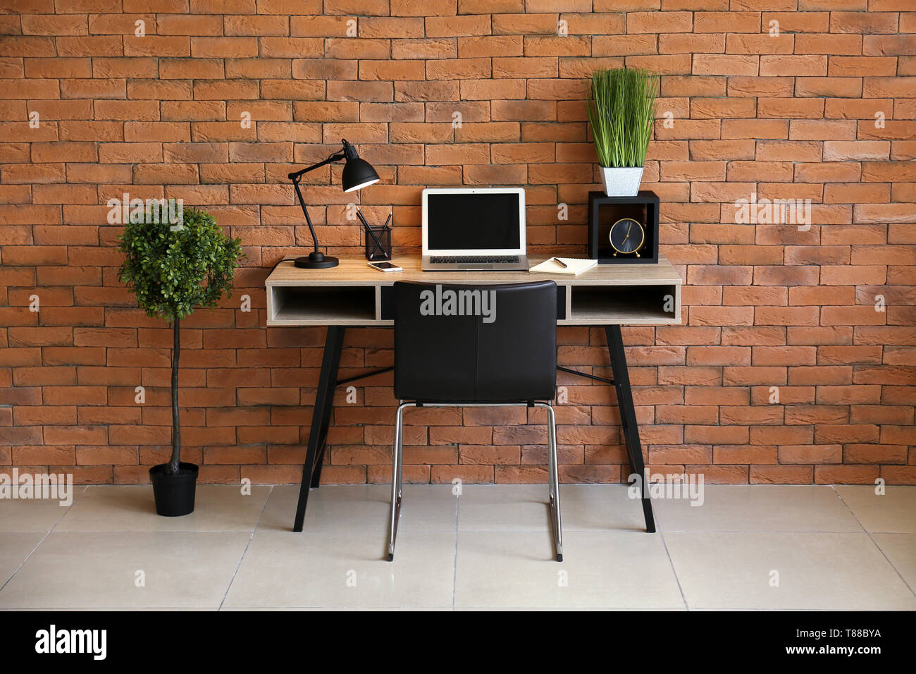 Stylish Workplace With Laptop On Table Near Brick Wall In Office