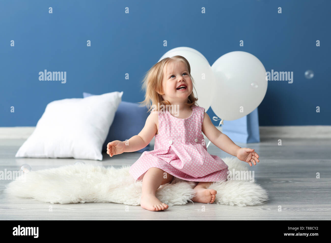 Cute Little Girl With Air Balloons Sitting On Rug In Room