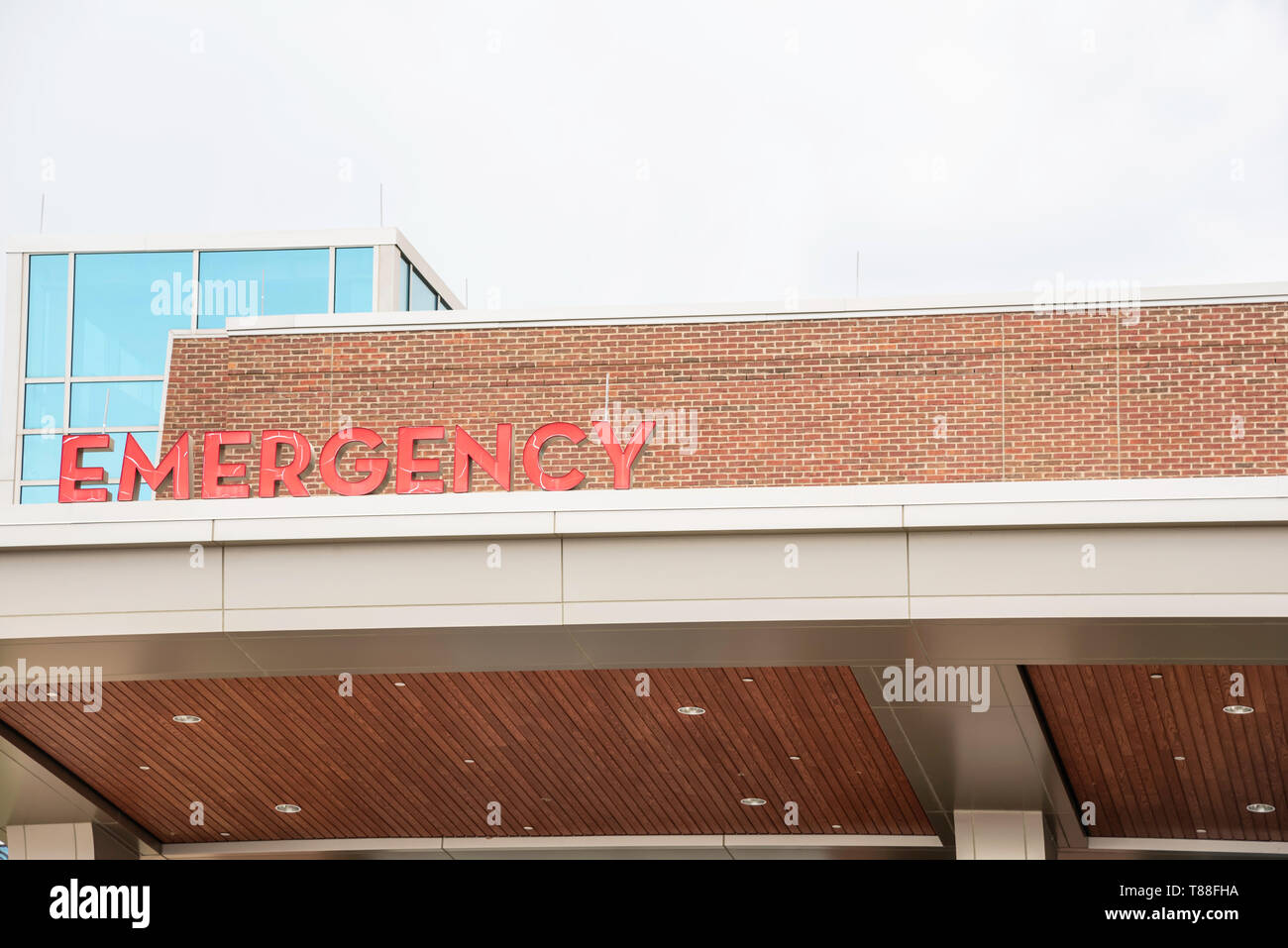 A prominent red 3D all-caps lighted emergency directional sign and marker perched on the awning and canopy of the main hospital entrance. Stock Photo