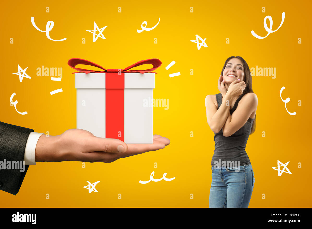 Young brunette girl wearing casual jeans and t-shirt smiling and touching face with big gift box in male hand on yellow background Stock Photo