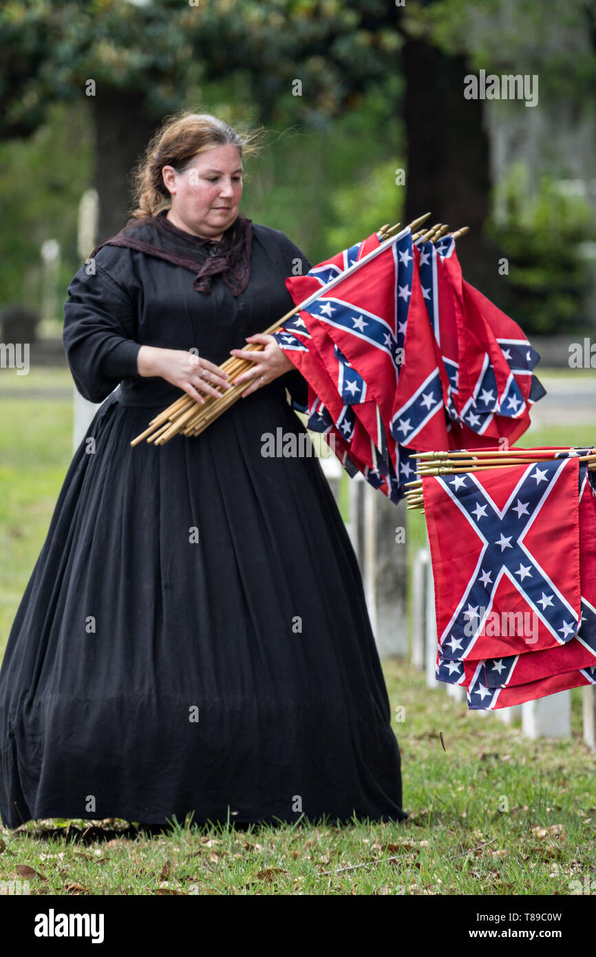 Charleston, USA. 11th May, 2019. A member of the United Daughters of the Confederacy, dressed in period costume, collects battle flags from grave markers during Confederate Memorial Day at Magnolia Cemetery May 11, 2019 in Charleston, South Carolina. Confederate memorial day continues to be an official state holiday in South Carolina where the American Civil War began. Credit: Planetpix/Alamy Live News Stock Photo