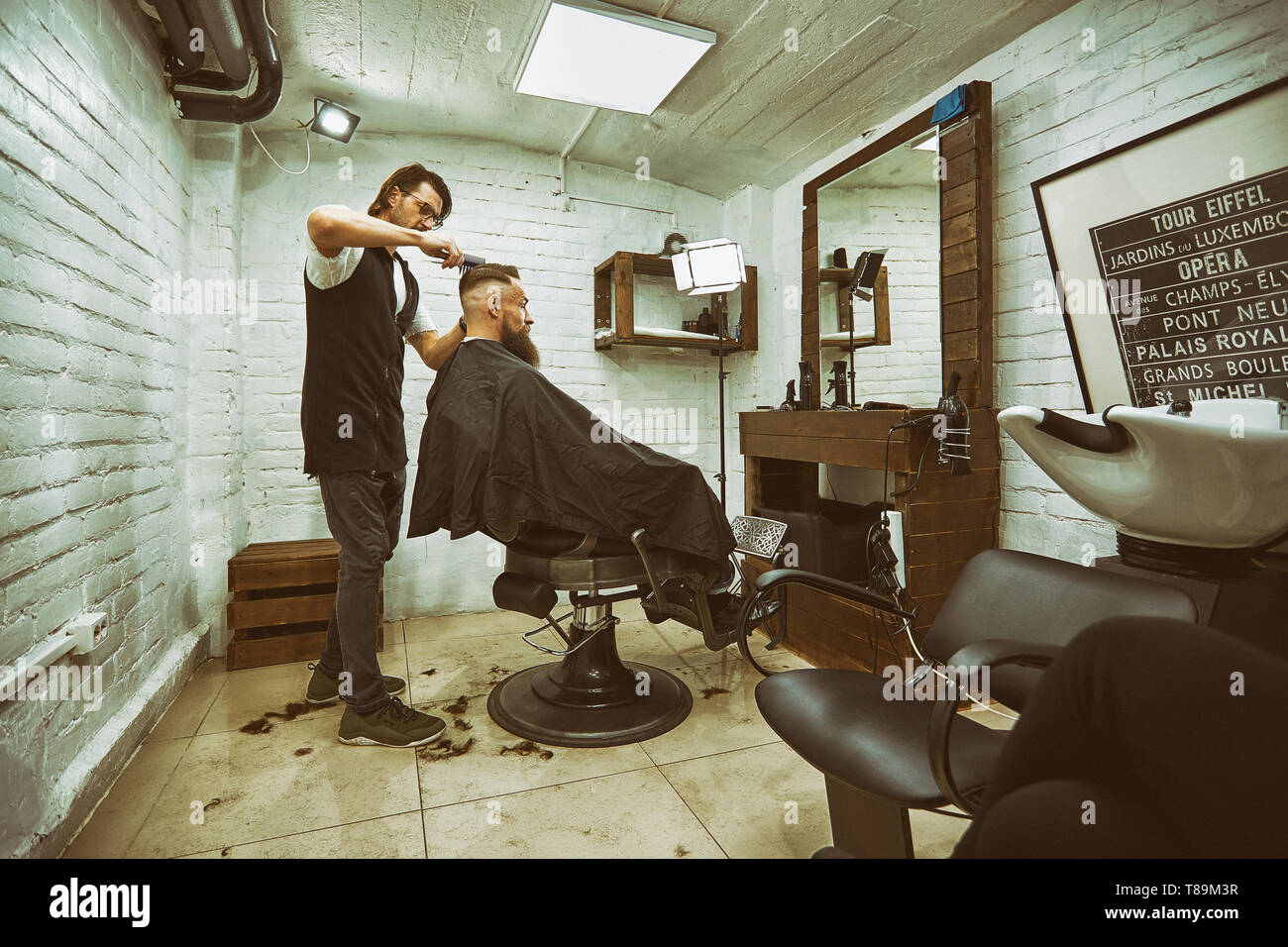 Brutal guy in modern Barber Shop. Hairdresser makes hairstyle a man with a  long beard. Master hairdresser does hairstyle by scissors and comb Stock  Photo - Alamy