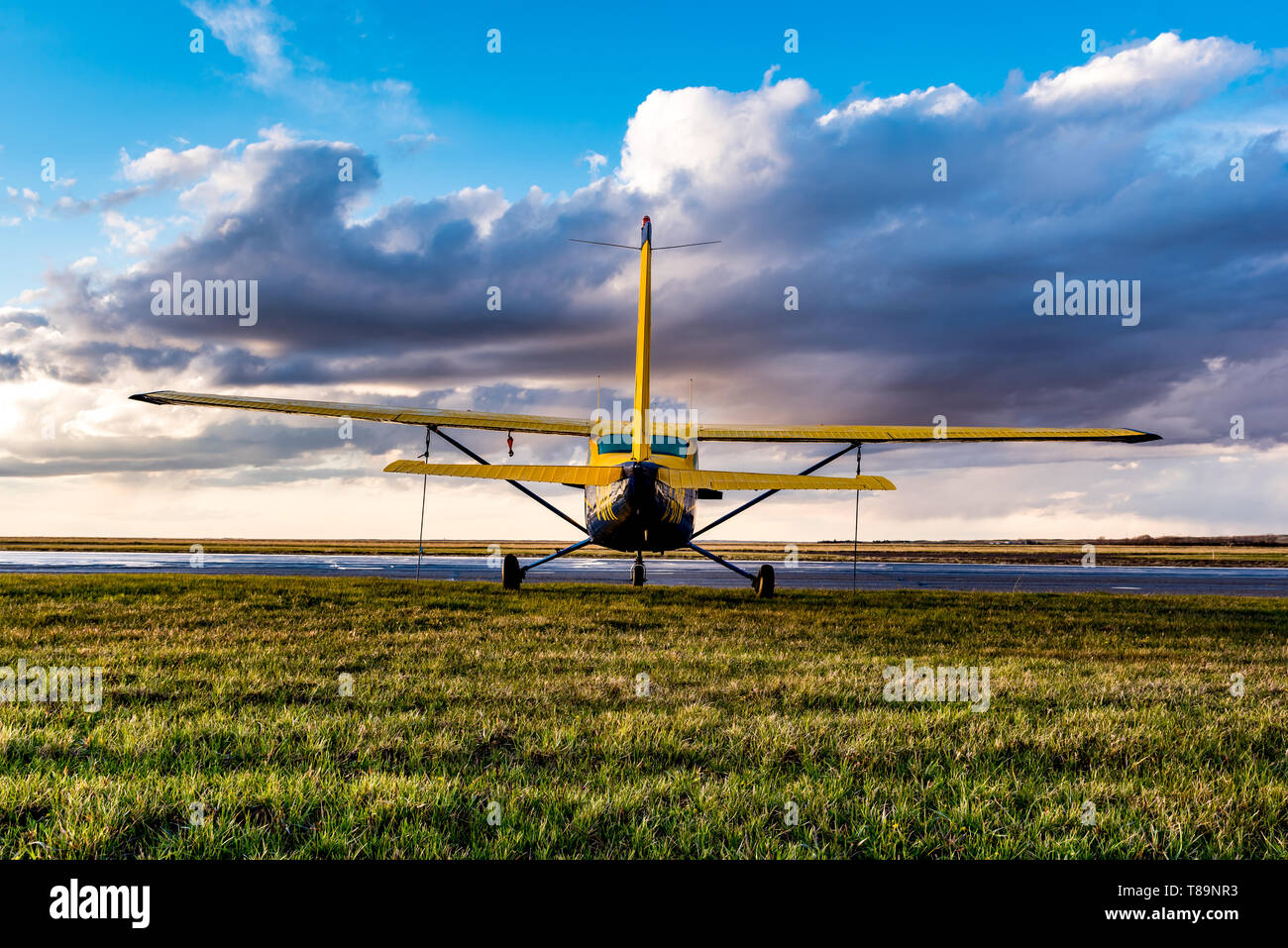 Swift Current, SK/Canada- May 10, 2019: Yellow Cessna Plane tied down in stormy skies Stock Photo