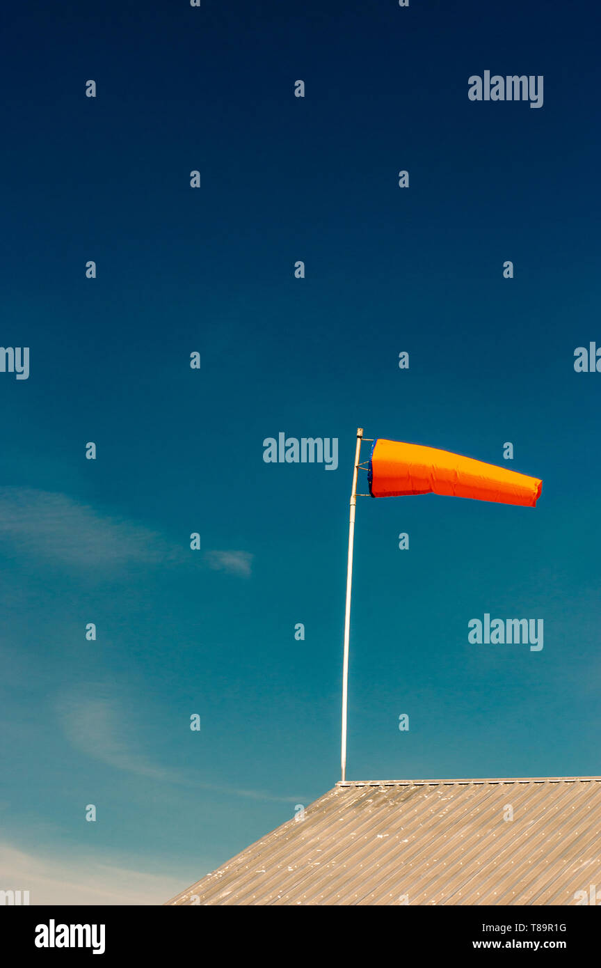 Horizontally flying orange windsock on metal rooftop and clear dark