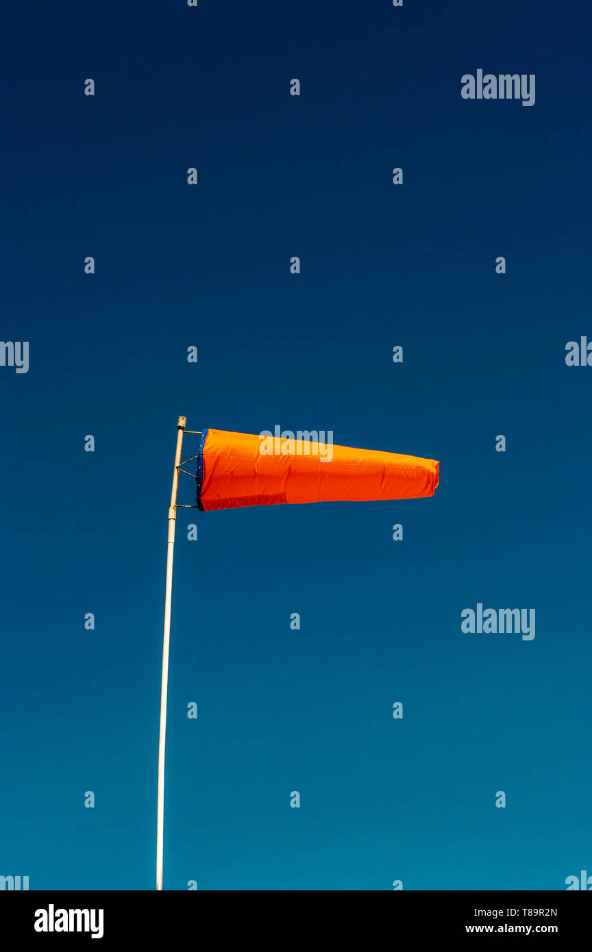 Horizontally flying orange windsock and clear dark blue sky with copyspace. Stock Photo