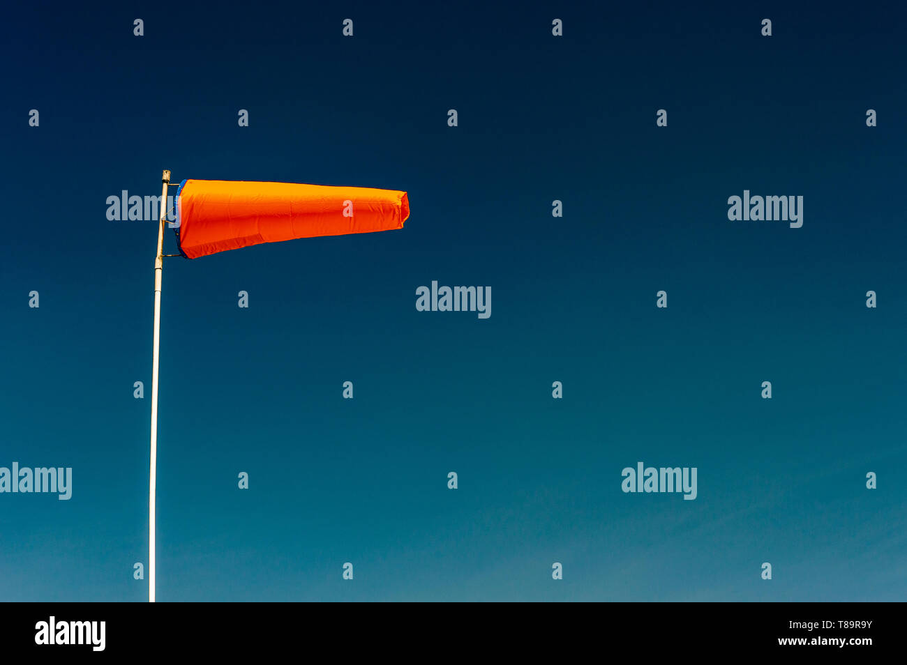 Horizontally flying orange windsock and clear dark blue sky with copyspace. Stock Photo