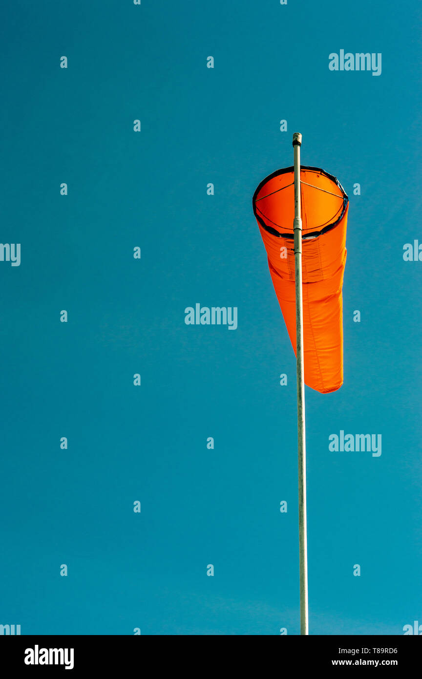 Downward angled plain bright orange windsock on white pole against a