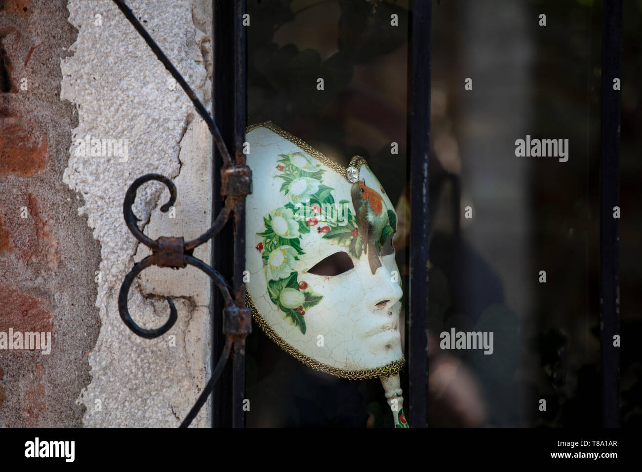 A traditional venetian mask worn during the Carnival season in a window in a quiet street in Venice. Stock Photo