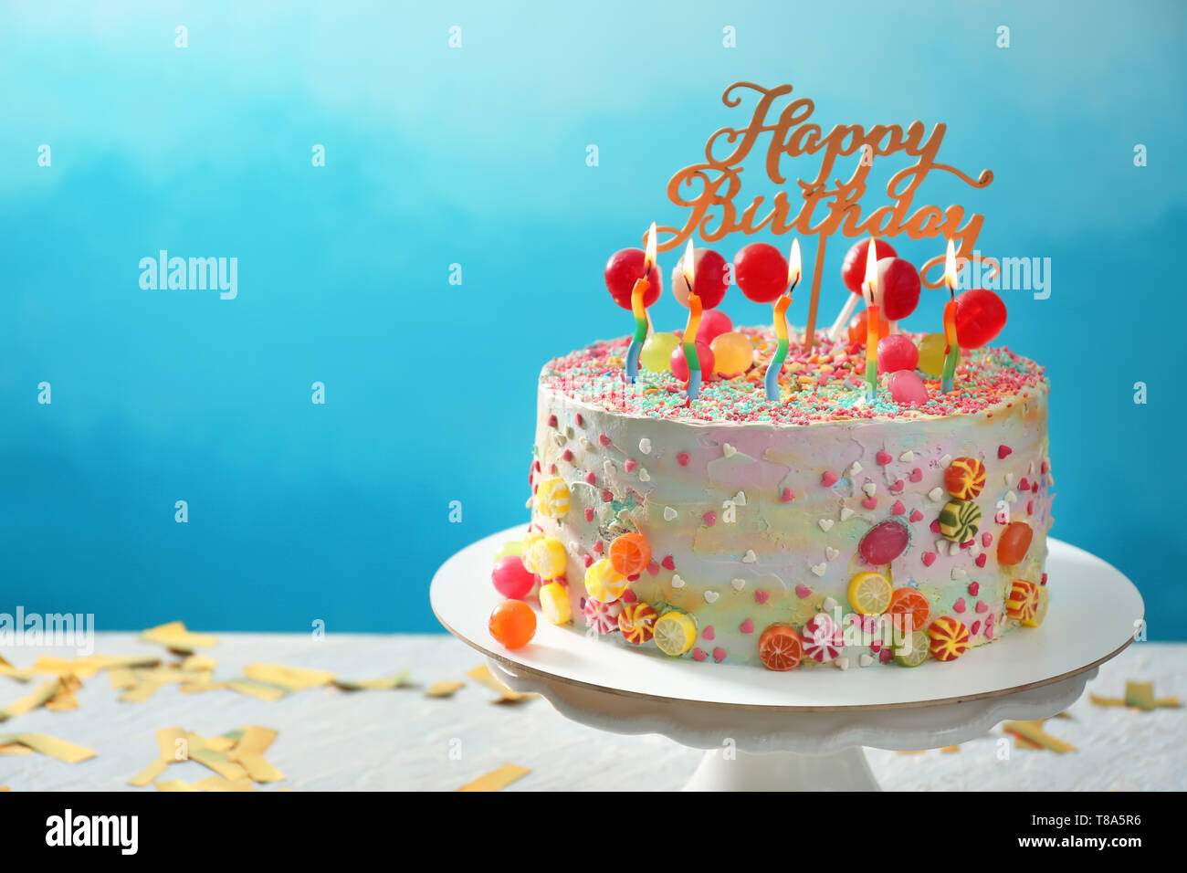 Stand with beautiful tasty birthday cake on table against color ...