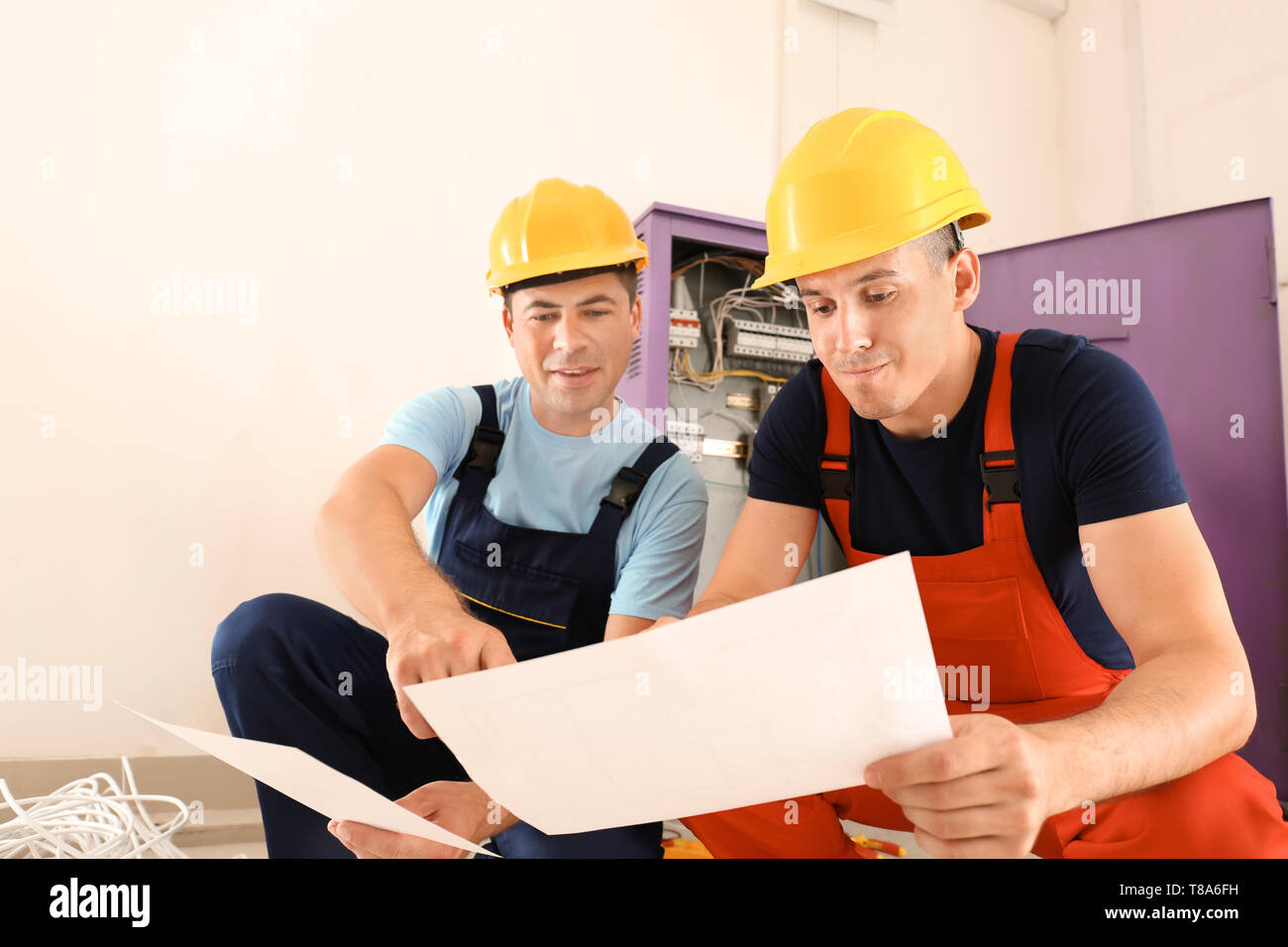Two electricians with house plan near distribution board indoors Stock Photo
