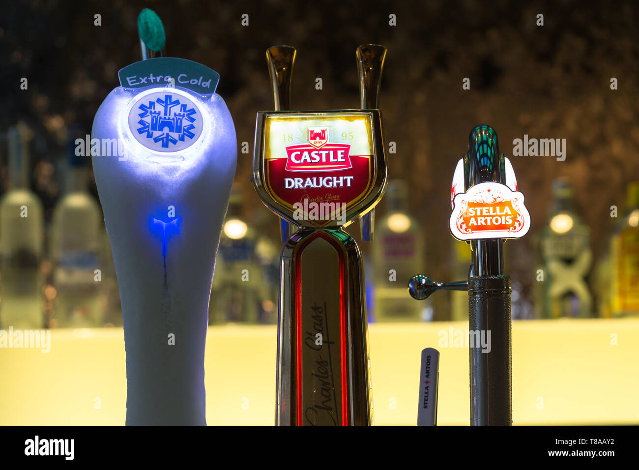 close up of illuminated draught beer taps or faucets for Castle and Stella Artois brands on a bar counter top in a hotel in Cape Town, South Africa Stock Photo