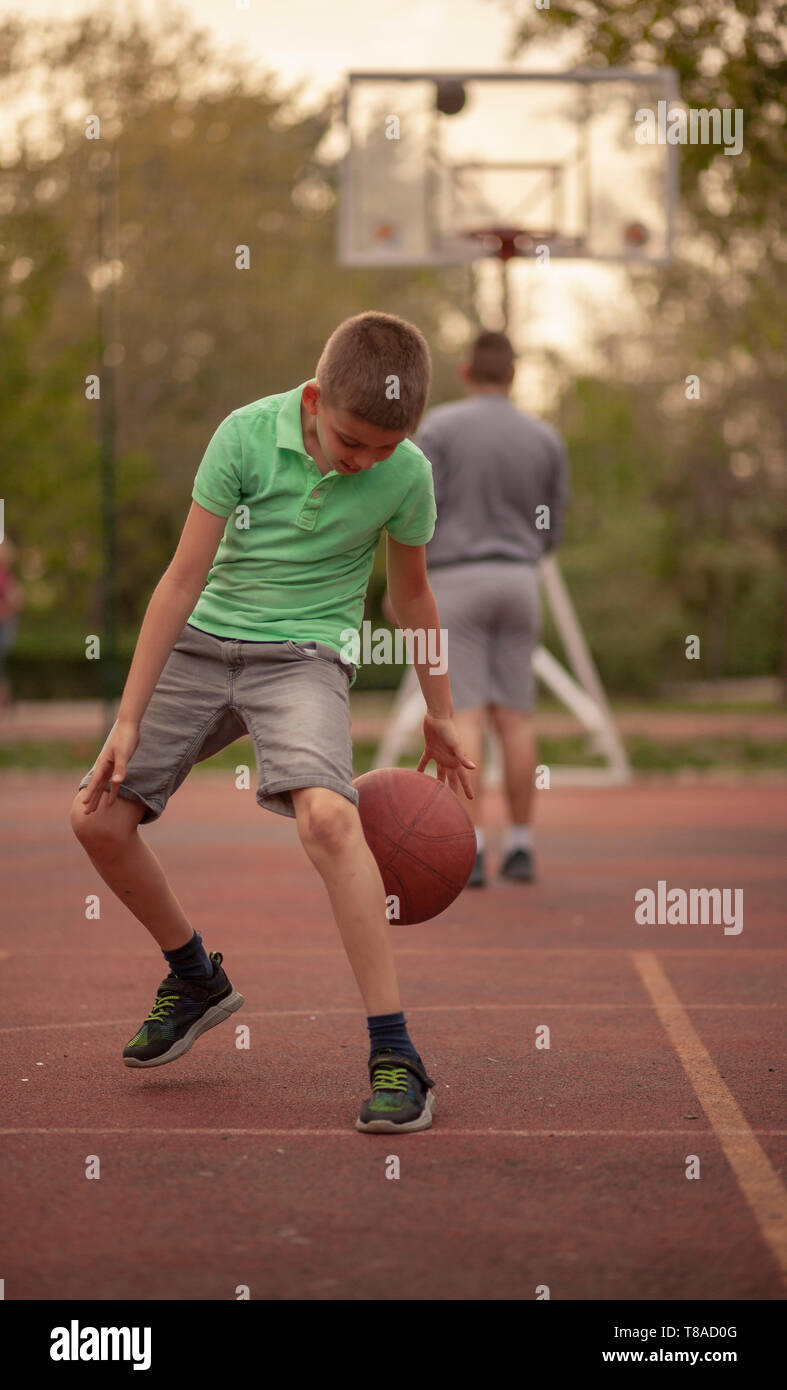 One boy, exercising dribbling ball between his legs. Outdoors on a