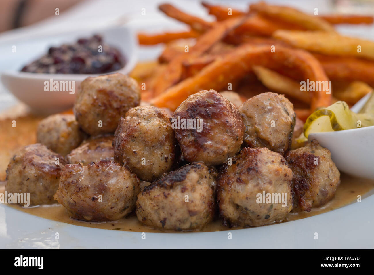 Kottbullar meatballs served with sweet potato fries, cucumber salad and lingonberry sauce Stock Photo