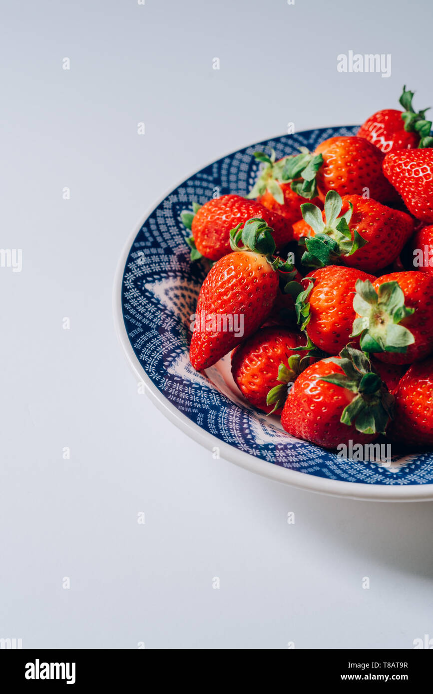 Fresh ripe strawberries in a blue and white plate, on the white table ...