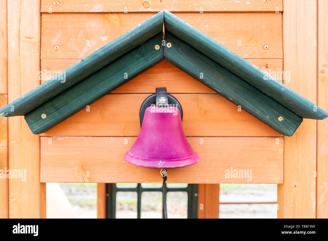 Pretend pink school bell on a wooden playground outdoors, with a string for making the ding dong noise, while kids participate in outdoor play. Stock Photo
