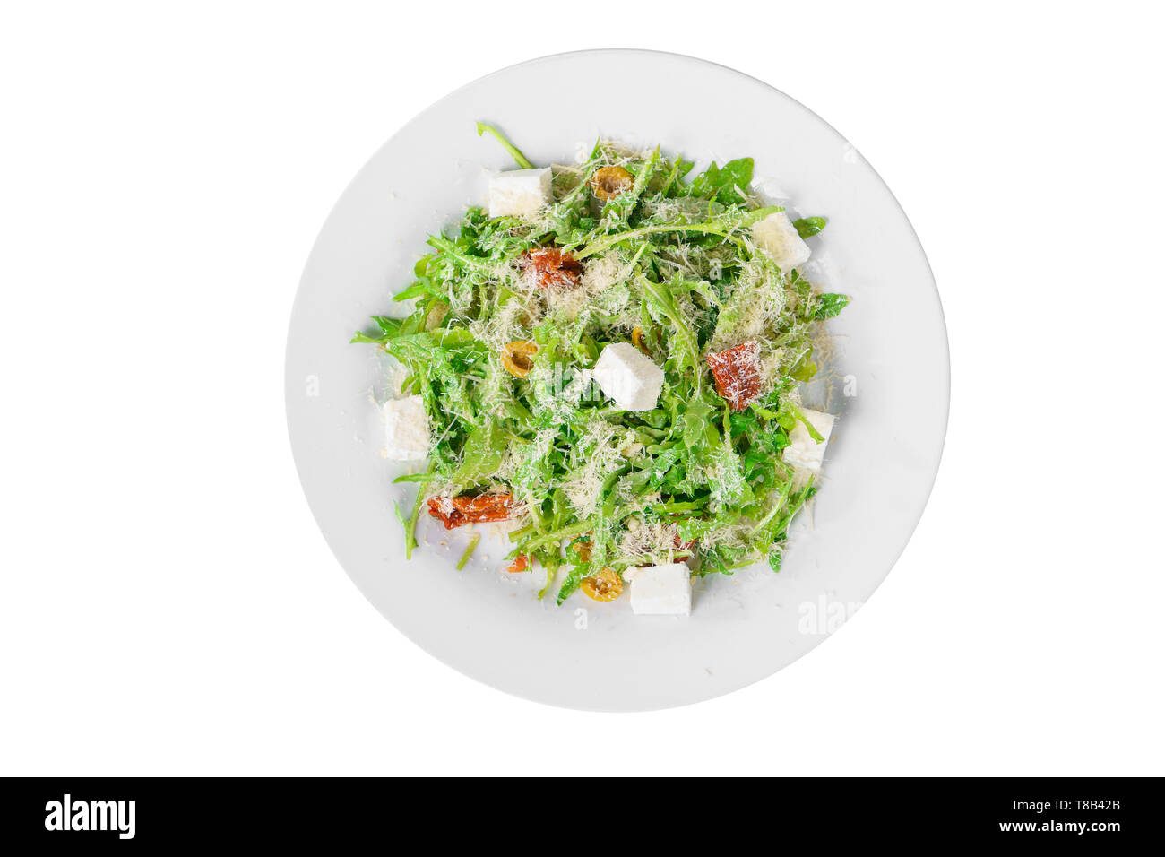 Salad with with arugula, feta, dried tomatoes, olives and grated cheese on plate, white isolated background, view from above Stock Photo