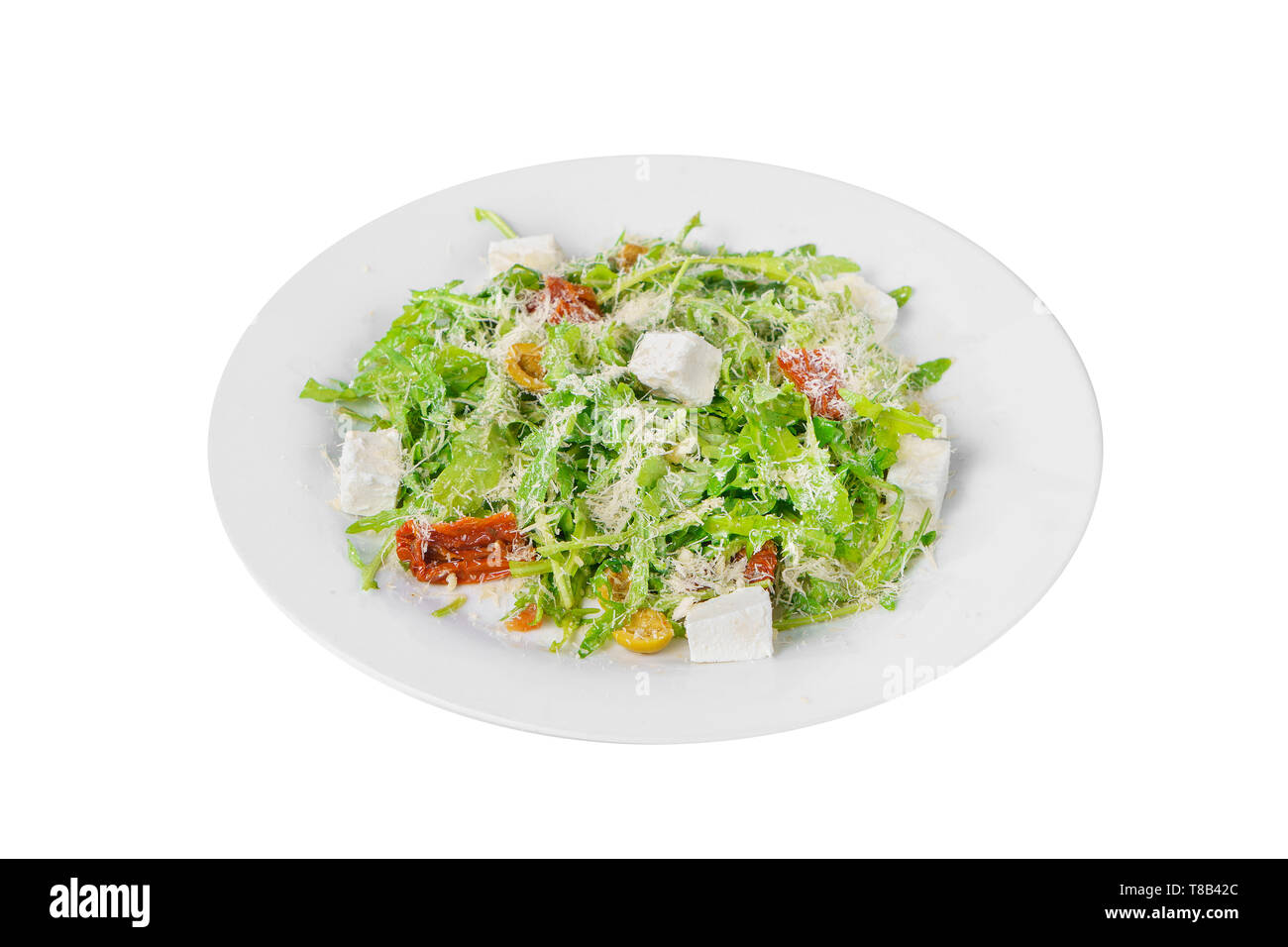 Salad with with arugula, feta, dried tomatoes, olives and grated cheese on plate, white isolated background, side view Stock Photo