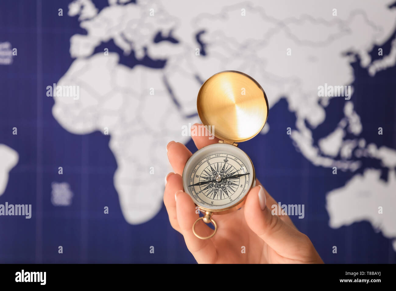 Woman holding vintage compass against blurred world map, closeup Stock Photo