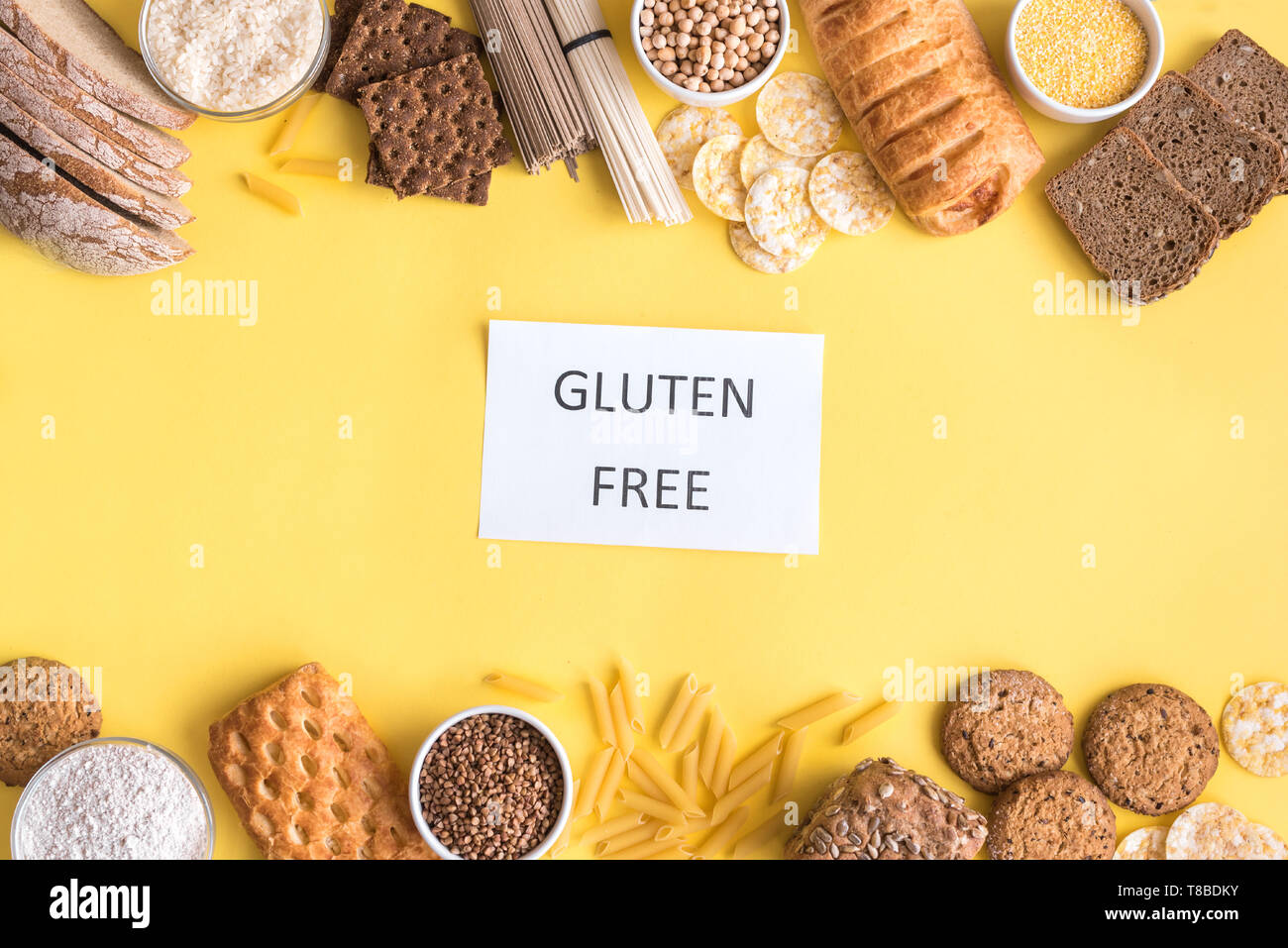 Gluten free food. Various gluten free pasta, bread, snacks and flour on yellow background, top view, copy space. Stock Photo