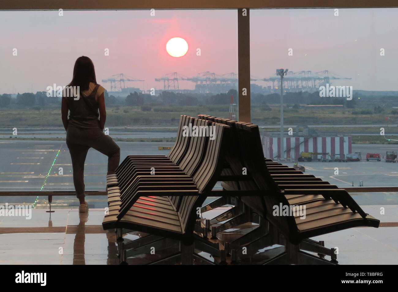 Girl contemplating the sunrise at a gate at the airport Stock Photo