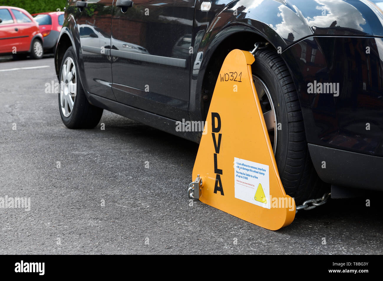 A car on a suburban street in the UK with a yellow DVLA wheel clamp
