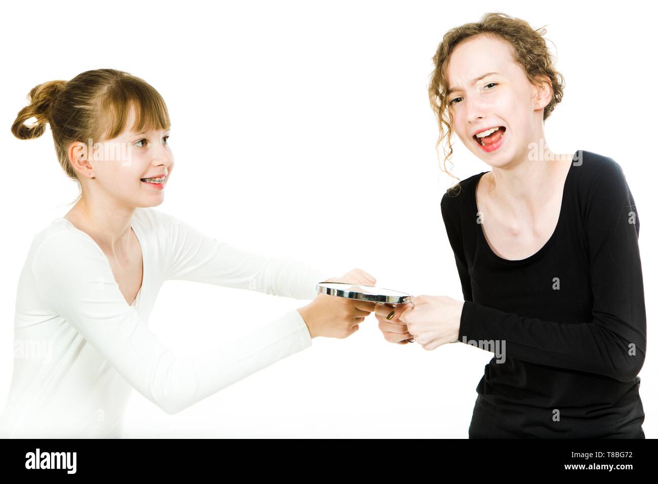 Two teenaged girls, one with braces, in puberty age haggle to get a mirror to make a make up - sister rivalry at home - white background Stock Photo