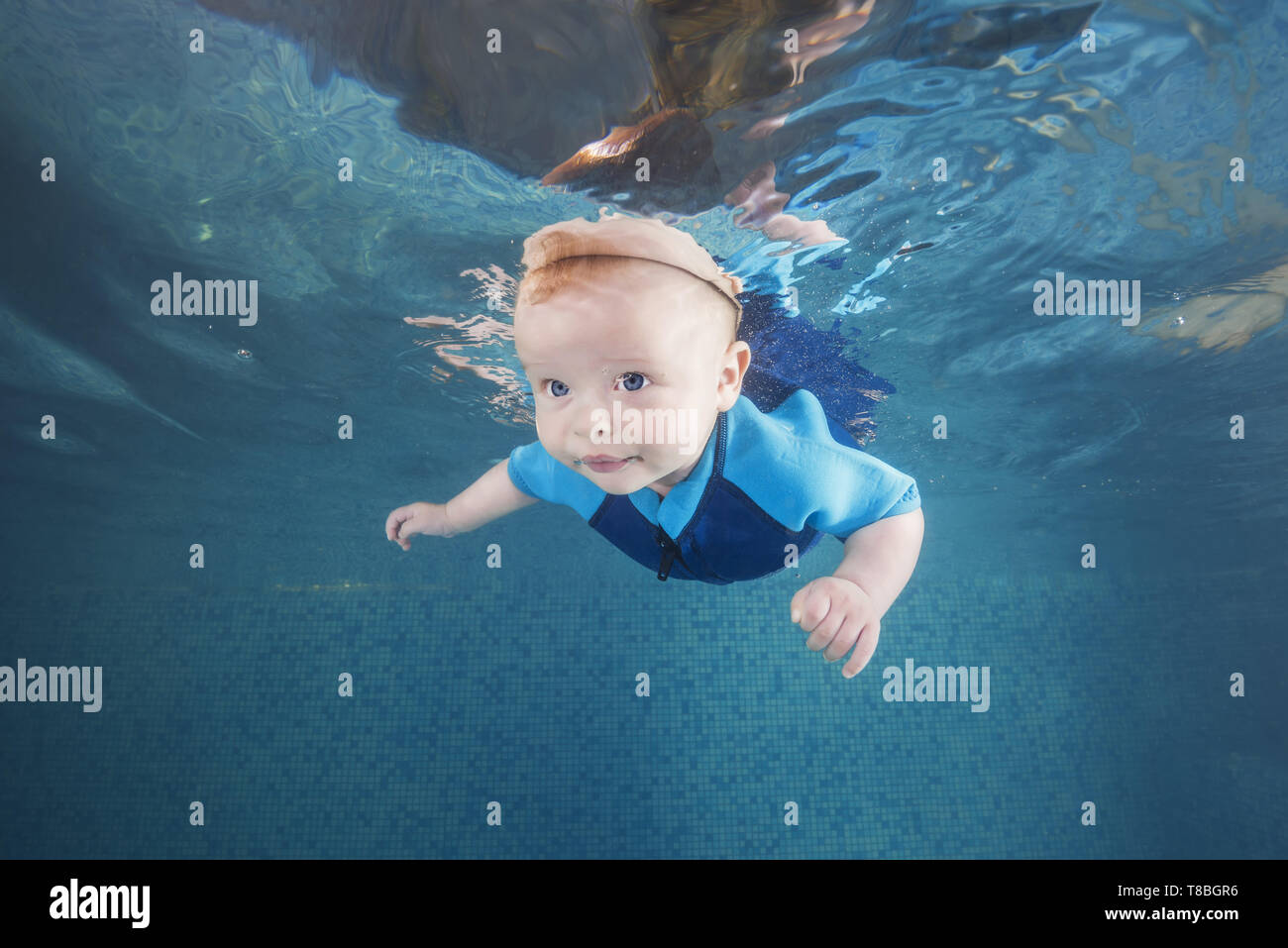 Little baby boy in a blue wetsuit learns to swims underwater in the