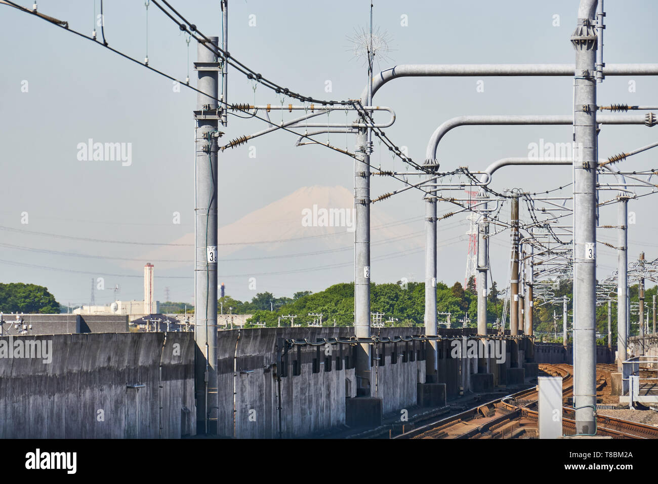 Mount Fuji is faintly visible in the distance over the train tracks of the Tsukuba Express Line at Moriya Station on a sunny morning. Stock Photo