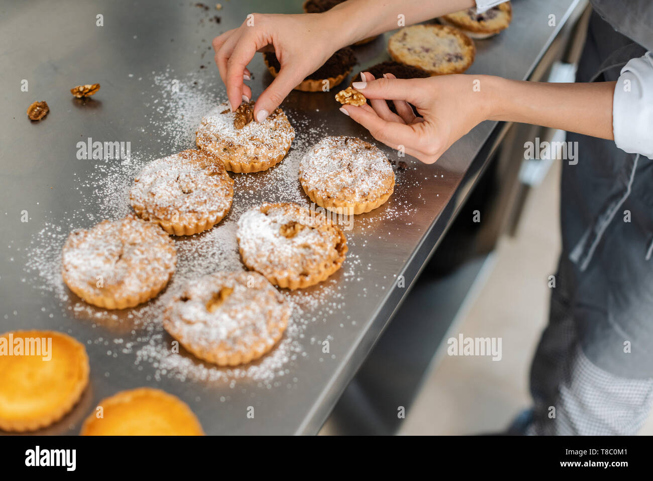 Confectioner putting nuts on little cakes Stock Photo