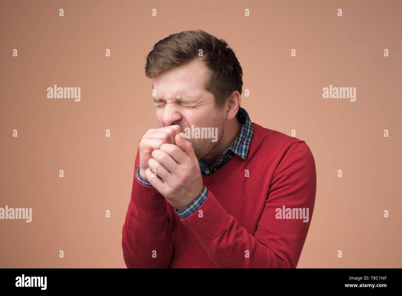 Handsome mature manin red sweater coughing a lot. Stock Photo