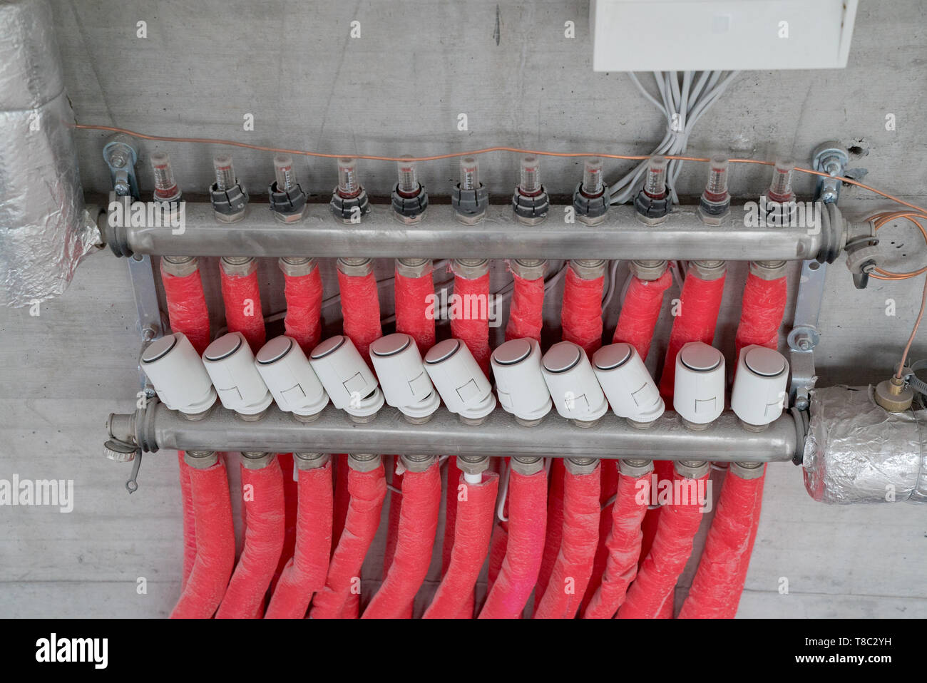 red floor heating pipes and valves at the regulation mains at an unfinished building site Stock Photo