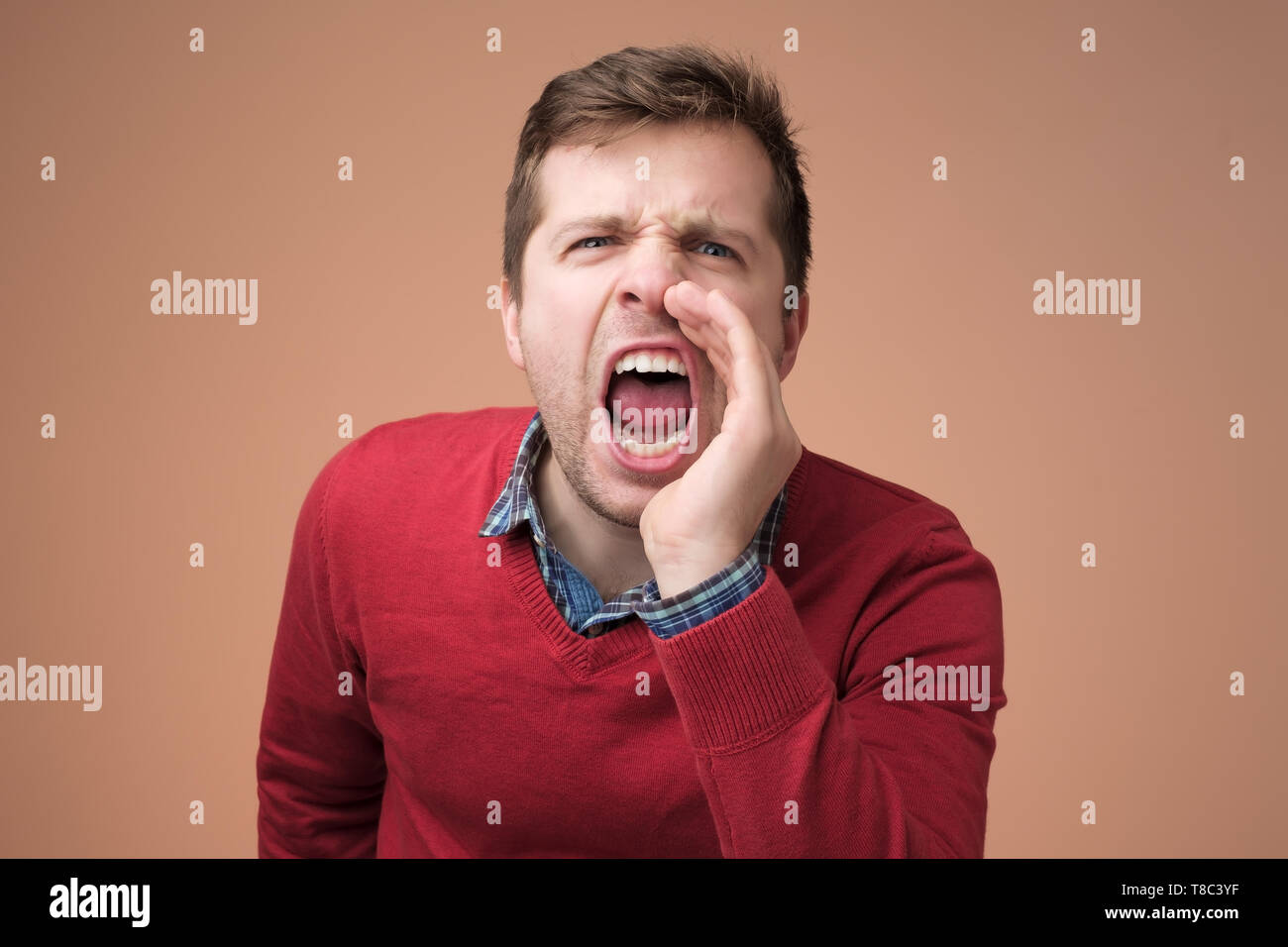 young man in red sweater shouting against brown background Stock Photo