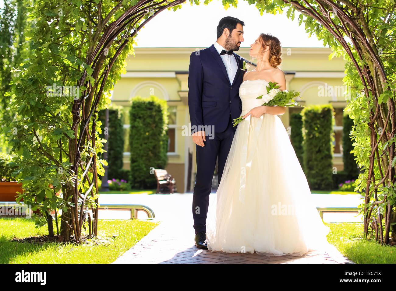 Happy wedding couple under floral arch outdoors Stock Photo - Alamy