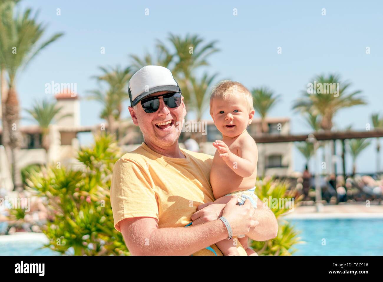 Happy father holding his cheerful son on holiday, resort with pool and palm trees as background, Portugal Stock Photo