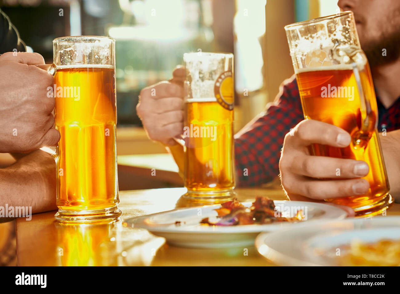 Selective focus of glasses of ale standing on table in pub. Strong male company keeping pints, drinking beer,  eating snacks and talking in bar. Concept of beverage and alcohol. Stock Photo