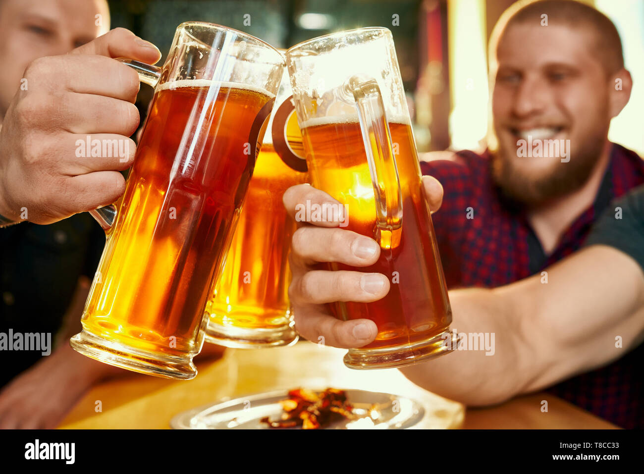 Closeup of glasses of beer in hands of happy company in pub. Cheerful male friends keeping pints of ale, toasting and laughing in bar on weekends. Concept of vacation and beverage. Stock Photo