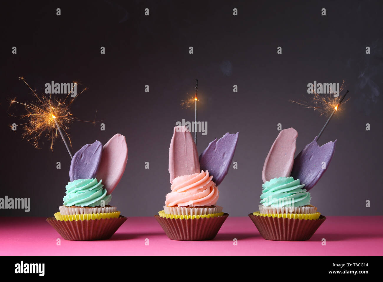 Delicious birthday cupcakes with sparklers on table against dark background Stock Photo