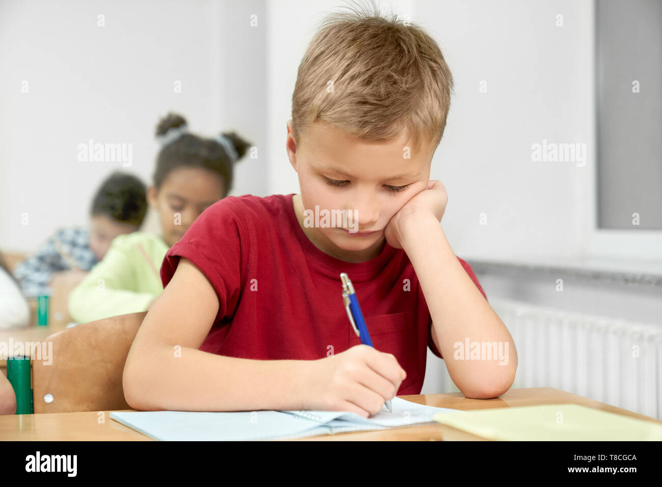 Primary Schoolboy Sitting At Desk Looking Down Leaning Head On