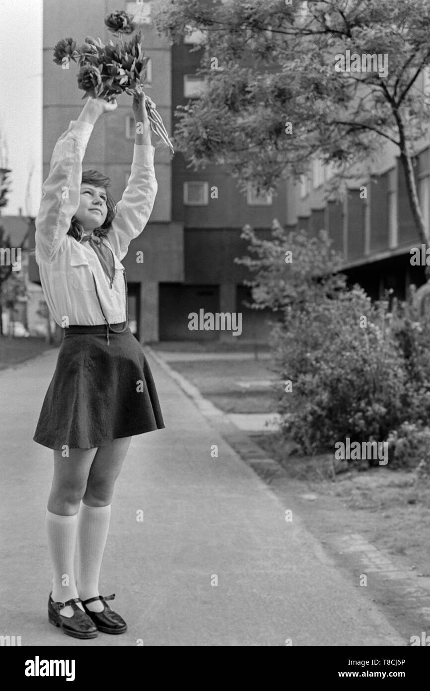 young schoolgirl member of the pioneer movement wearing her necktie and uniform while waving a bunch of flowers in the street 1970s hungary Stock Photo