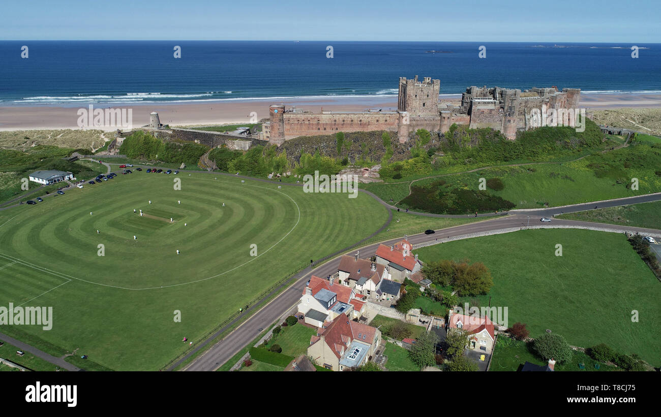 Bamburgh cricket team play their first match of the season against Ellingham in the shadow of Bamburgh Castle in Northumberland. Stock Photo