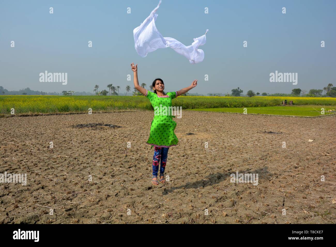 A girl wearing a salwar kameez flying a white dhupatta / clothin the air in a field on a bright day, selective focusing Stock Photo