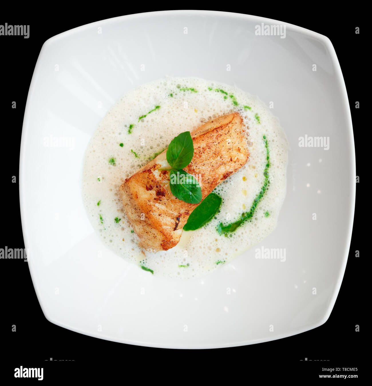 Braised fish fillet with froth sauce shot from above isolated on black Stock Photo