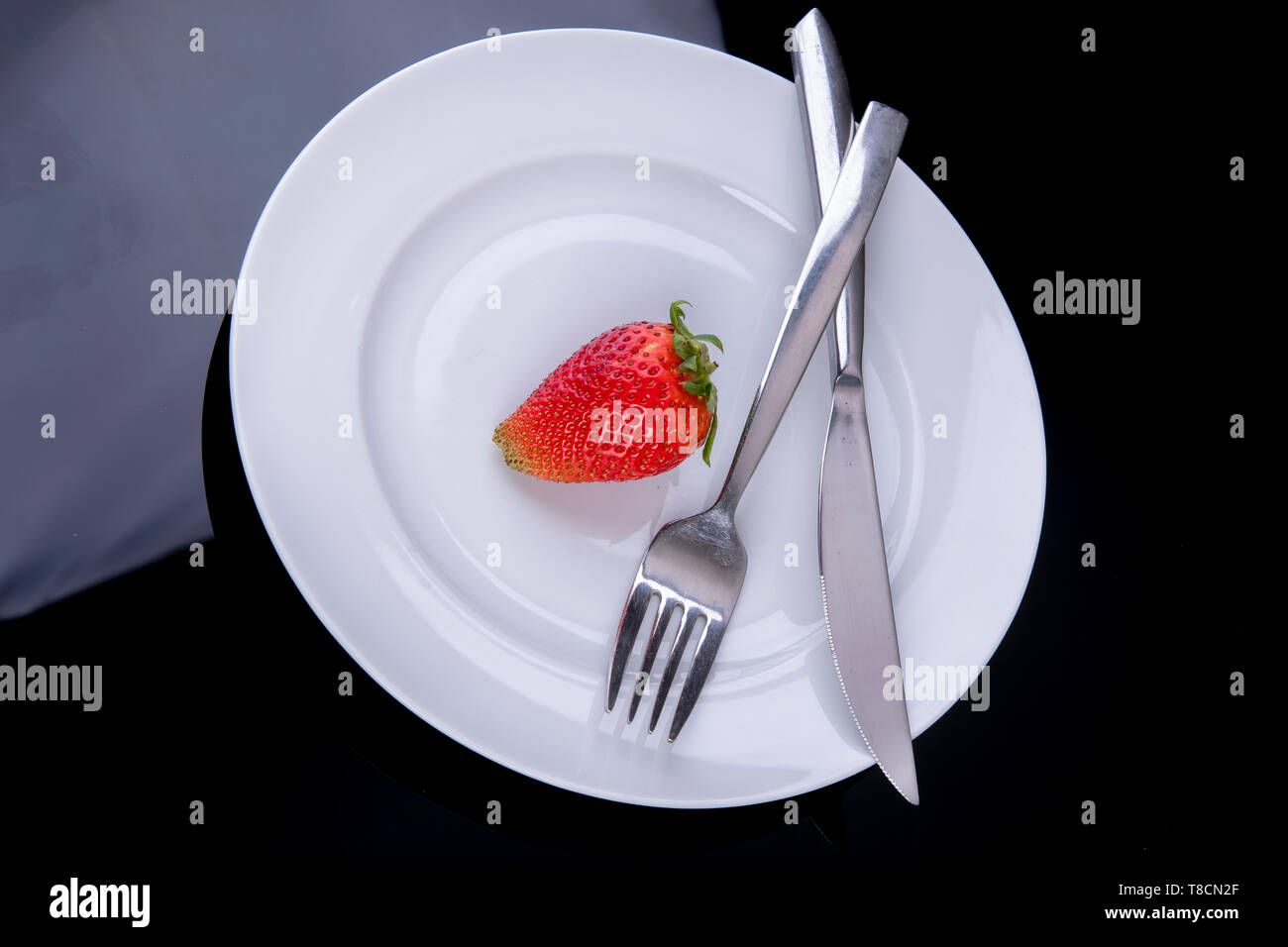 lonely strawberry on a white plate with cutlery as diet plan Stock Photo