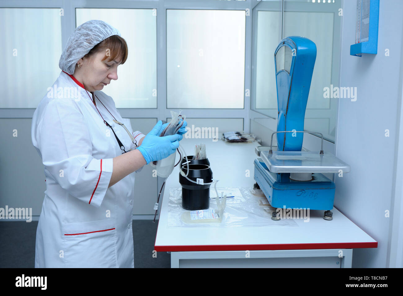 Nurse standing near a table with scale holding containers with blood