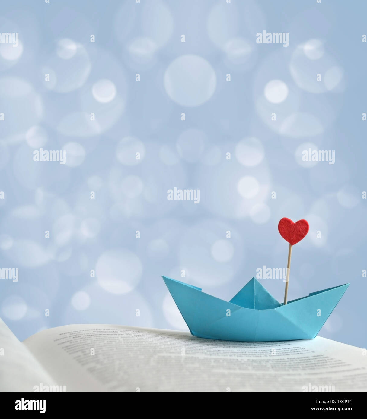 The photo blue paper boat with a red heart on the page of the book, there is space for text. Can be used as a template, romantic greeting card, poster Stock Photo