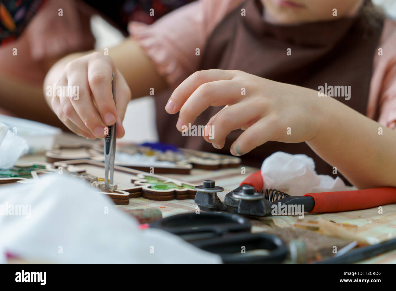 The artist maker mosaic in a wooden harvesting. Child hands closeup collect mosaic of colored stones. Human activity to workplace Stock Photo