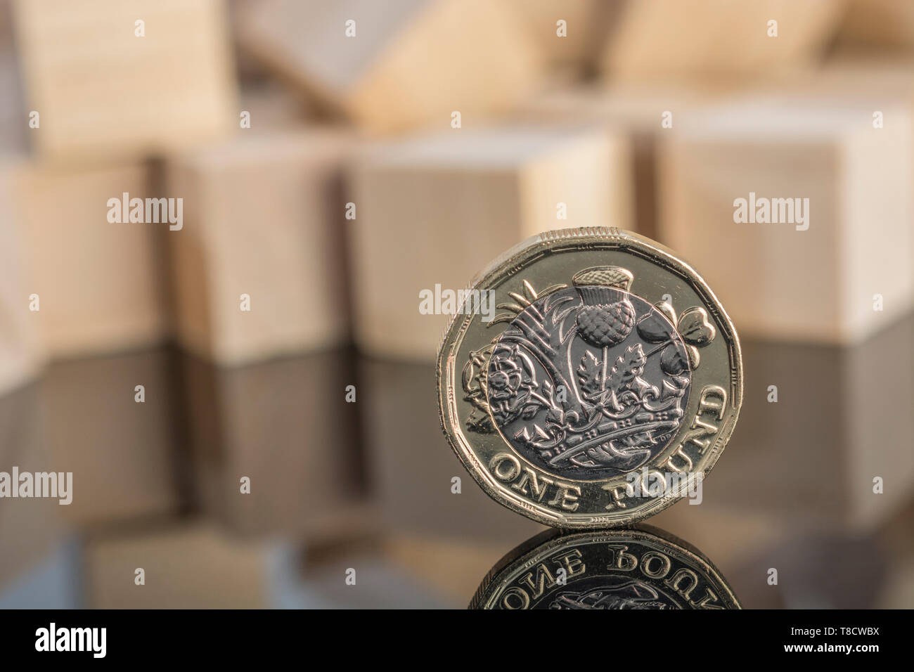 UK New Pound coin on reflective background with scattered wood bricks.For Pound collapse, Sterling collapse, fall in Pound value, UK banking crash. Stock Photo
