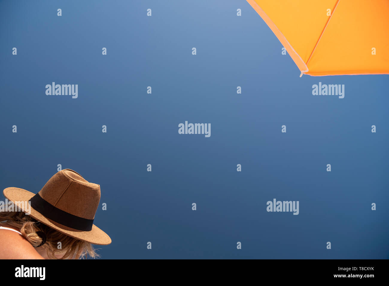 A holidaymaker wearing a hat and sitting under an ambrella Stock Photo