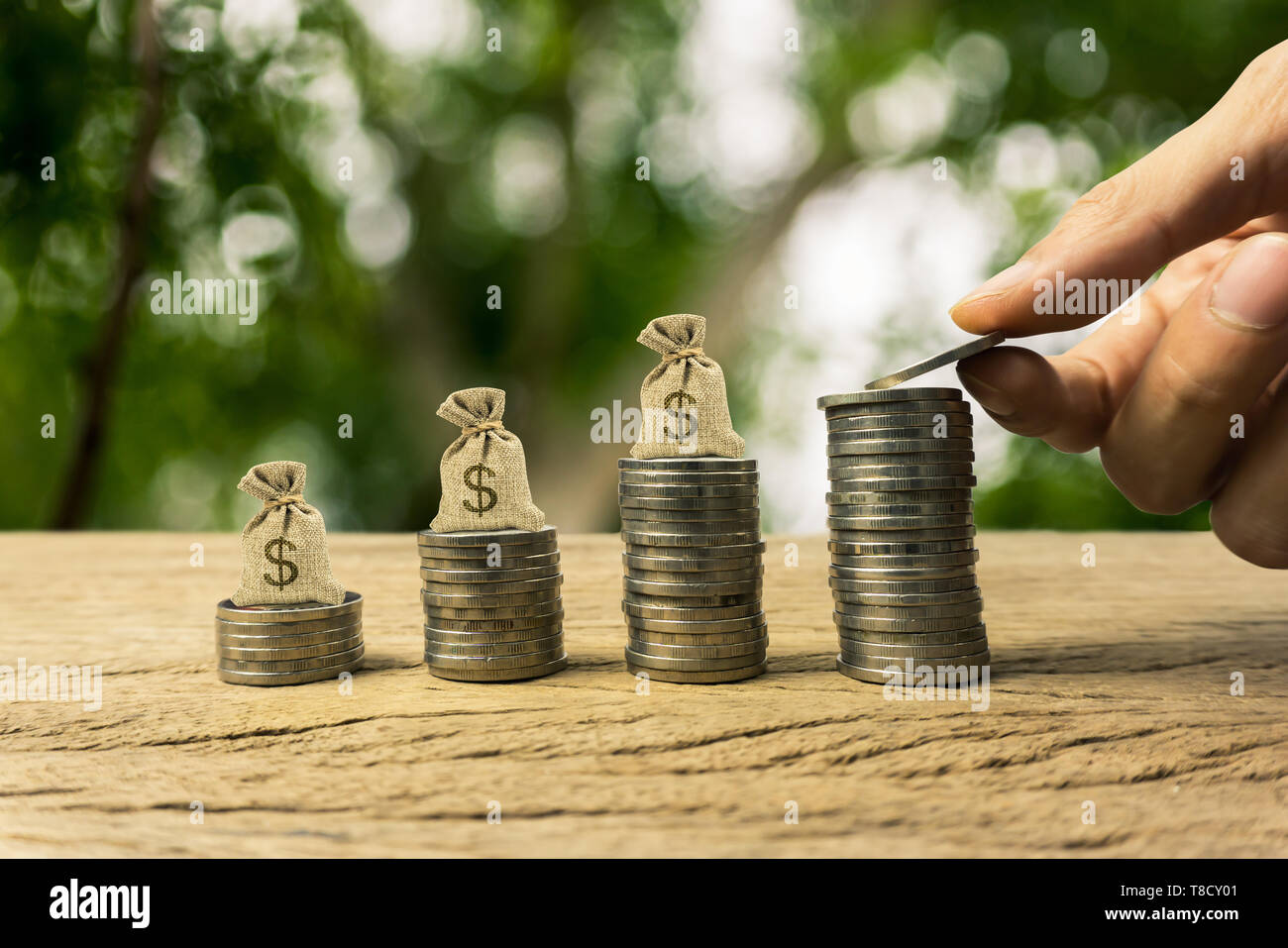 Growing time value of money, investment, wealth financial concept. Hand holding coin, and US dollar bags on rising stacked coins, term sustainable fun Stock Photo